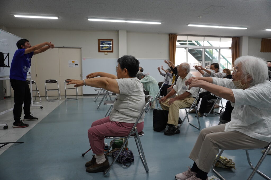 塚本さんと一緒に手を伸ばしている会員さん