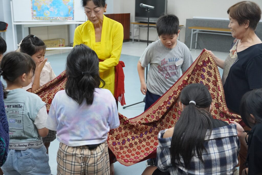 先生がバリの生地を広げ、それを見て触っている小学生たち