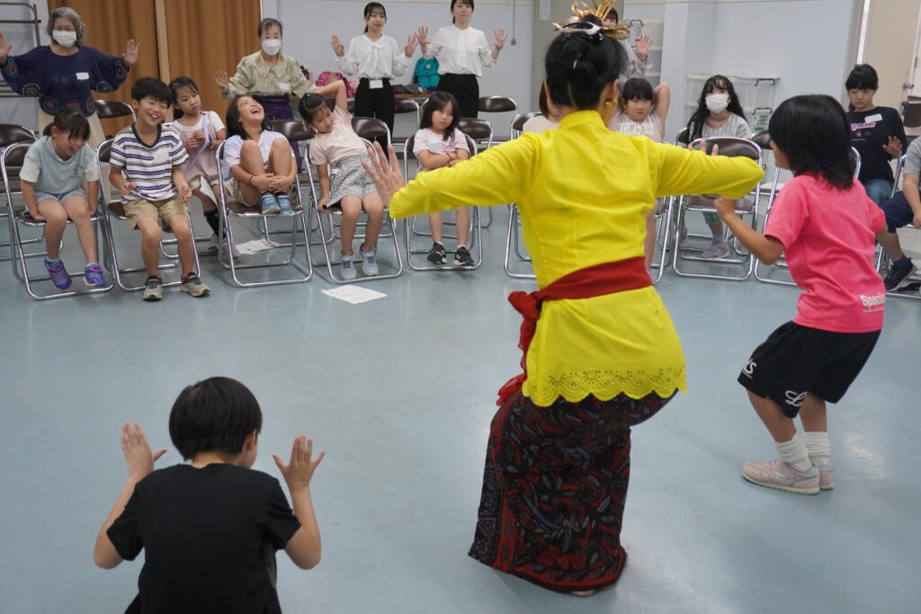 バリ舞踊を踊る先生と小学生たちの後ろ姿と、小学生たちと藤枝市の担当の方と大学生たち