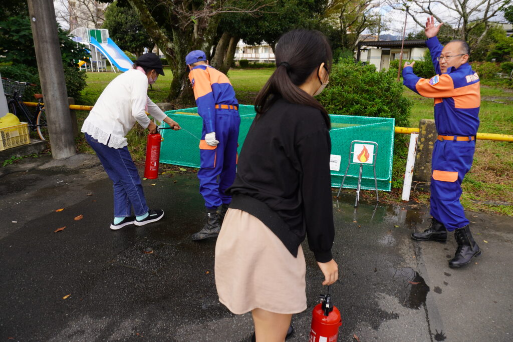 消火訓練をしている参加者と、説明している消防団員