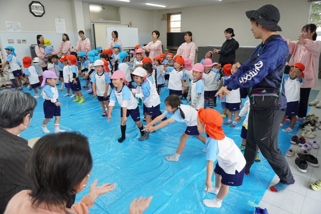 お遊戯を披露する園児と、見守る会員達