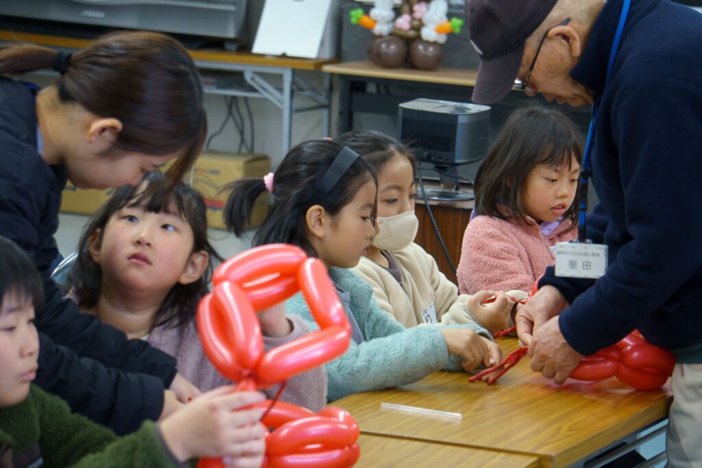 サポーターに手伝ってもらいながら、バルーンをねじる子どもたち