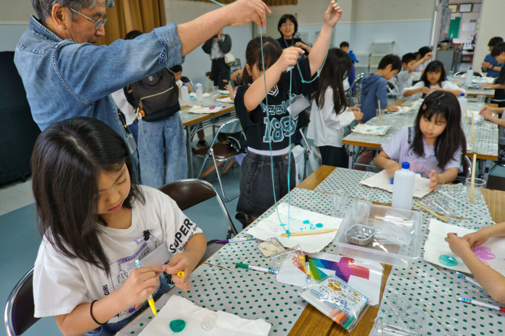 色をつけたスライムを伸ばす子どもとサポーター