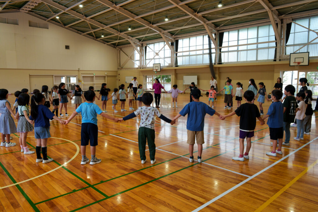 手をつないで一つの大きな円になる子どもたちと先生