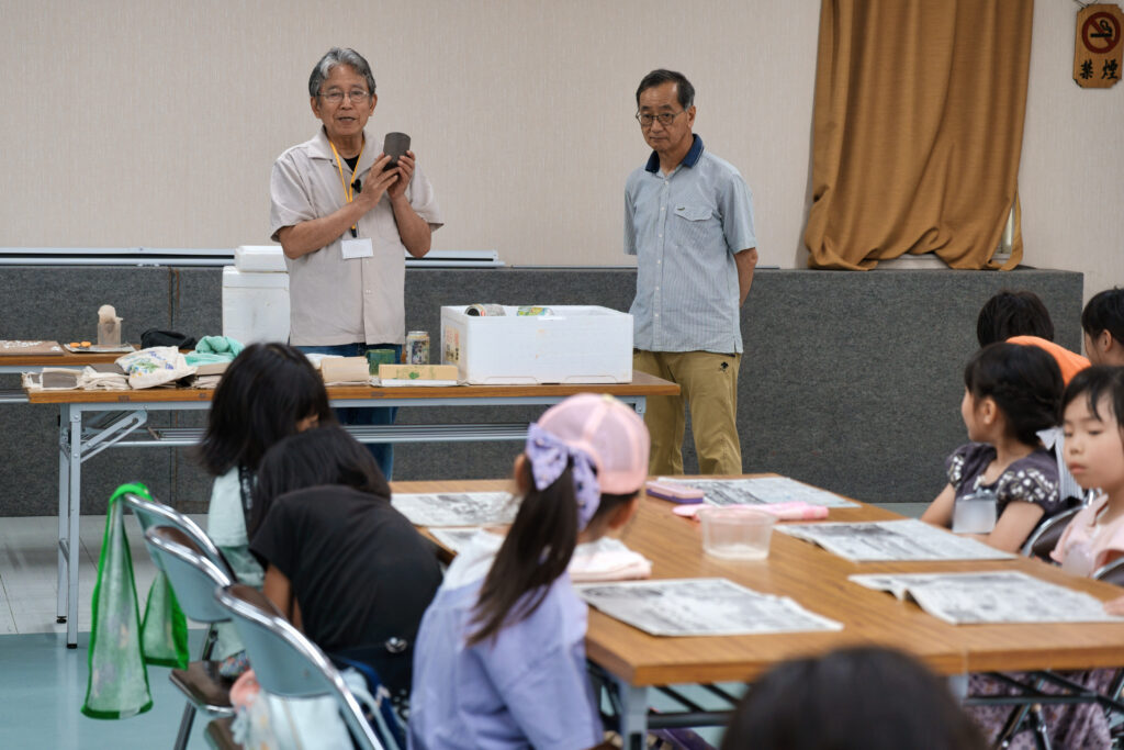 お手本を使い説明する先生と、それを聞く子どもたち