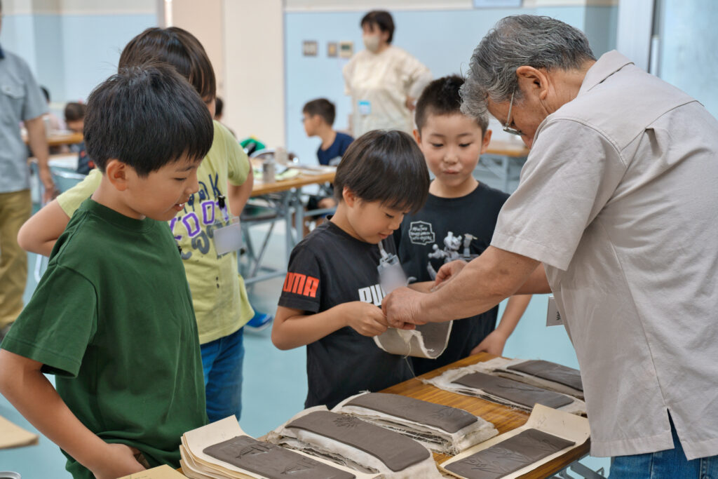 模様がついた粘土板を選ぶ子供たちと、手渡す先生