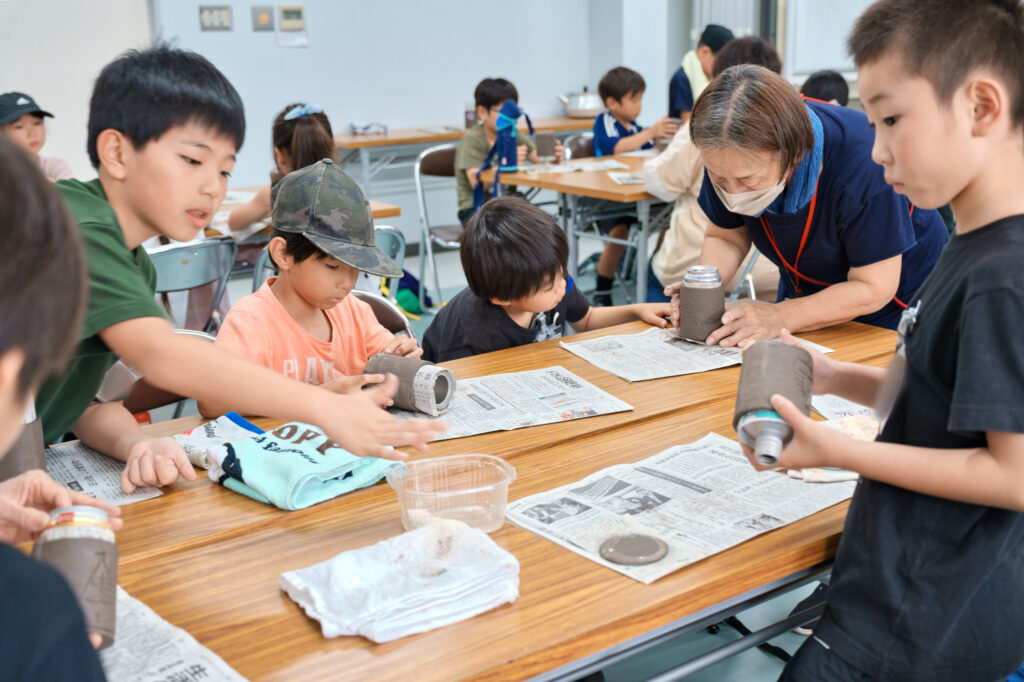 手に水を付け底を張り付ける子どもたちと、教える先サポータ