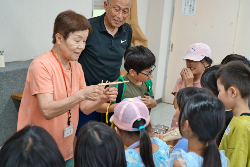 支援員に割り箸鉄砲の作り方を教わる子どもたち