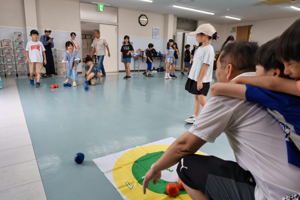 ボッチャを行う子どもたちと見守るサポータ、背中に子どもが乗っている