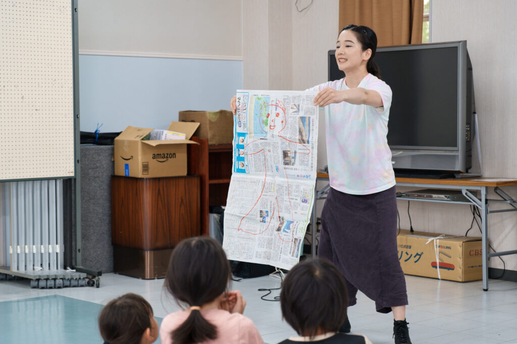人が描かれた新聞紙を広げて見せる宮城先生
