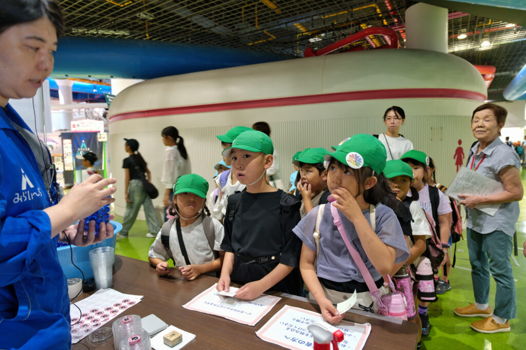 ビーコロ展入場口で職員の方から説明を受ける子どもたち