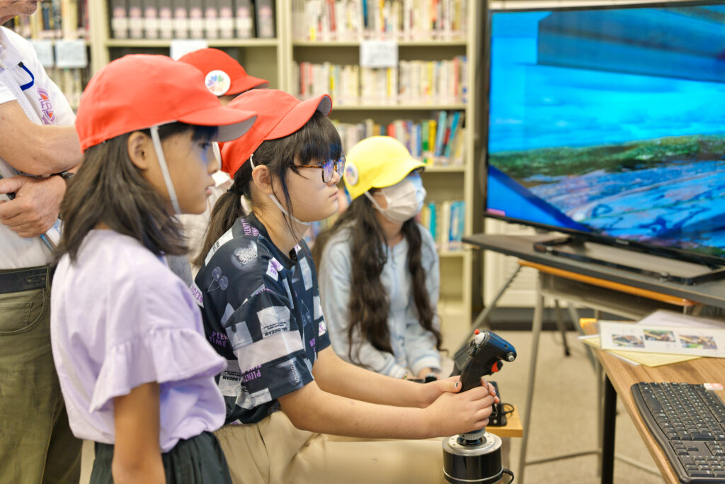 フライトシミュレーターを操作する子どもと、周りで見守る子どもたち