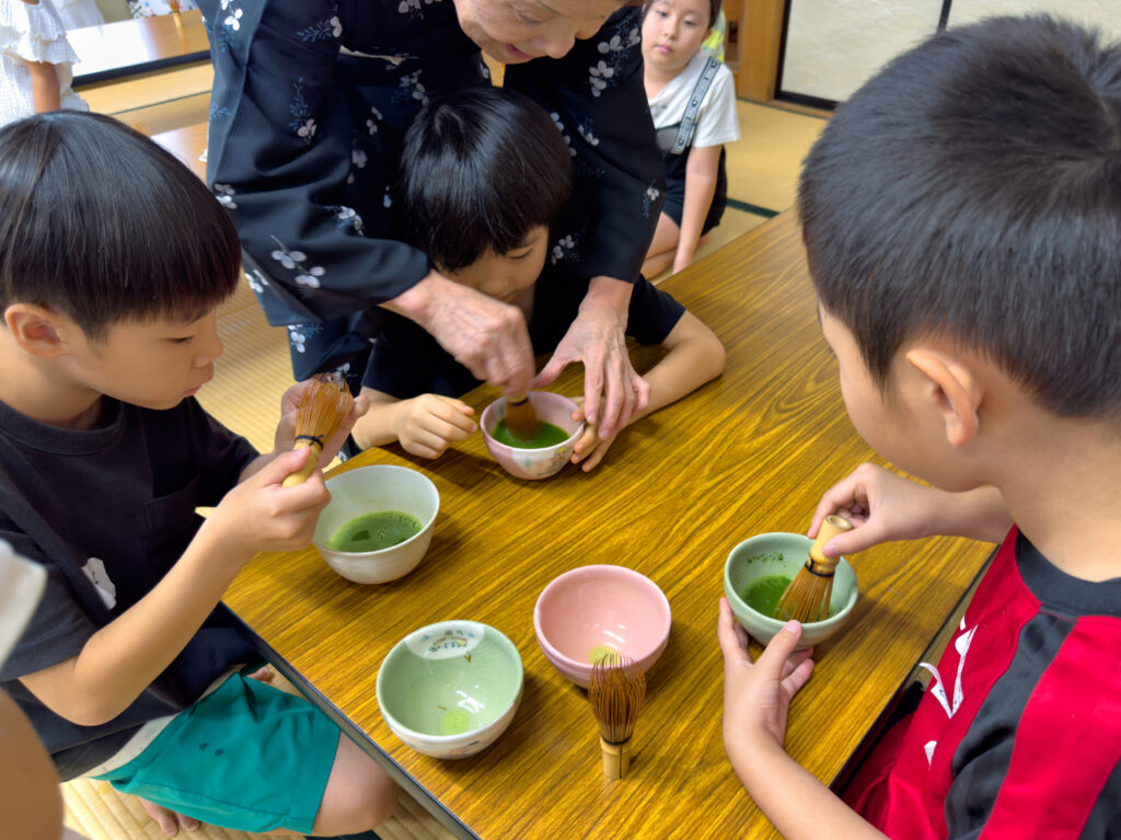 先生と一緒に抹茶を点てる子どもたち