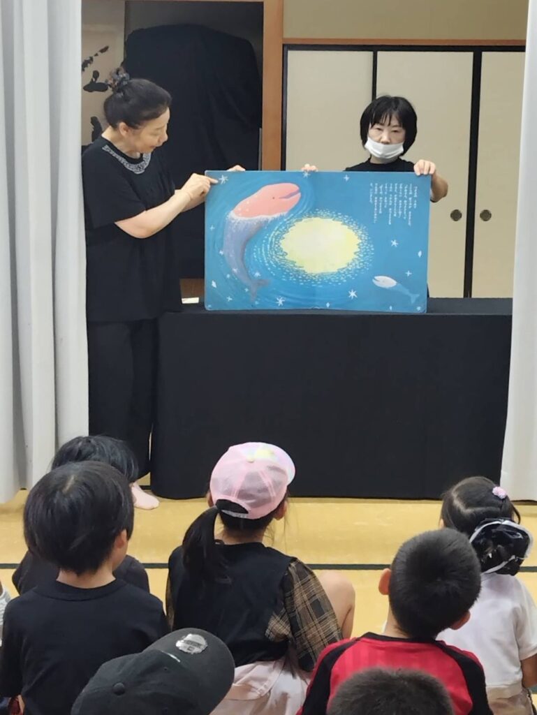 大型絵本を読む「ふしぎなたまご」の方々と、聞く子どもたち