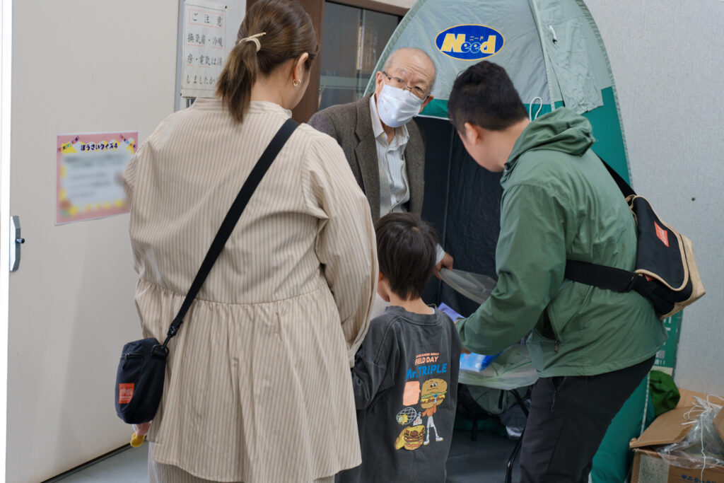 防災テントの解説をする防災委員と、解説を受ける親子