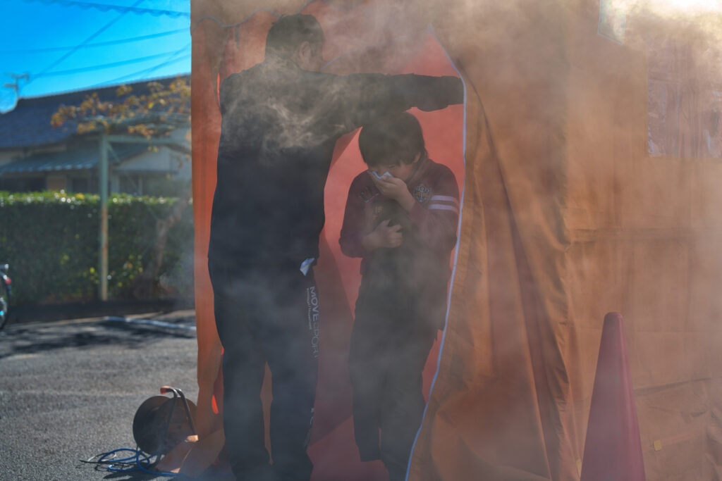 口をハンカチで覆った小学生がスモークハウスから出てくる