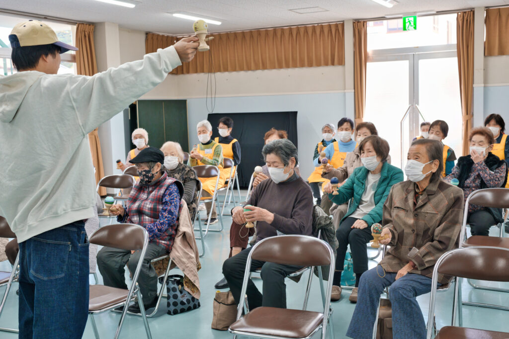 けん玉を手に持ち説明するぎんちゃんと、けん玉を手にした会員たち