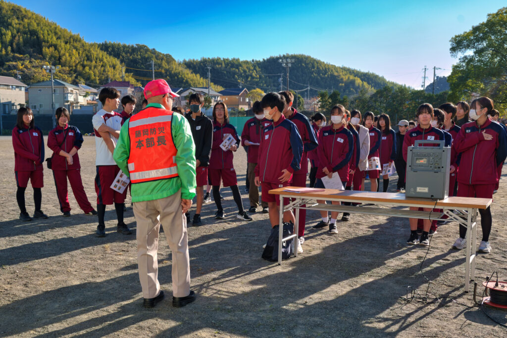 グラウンドで自治会長の挨拶を聞く小中学生