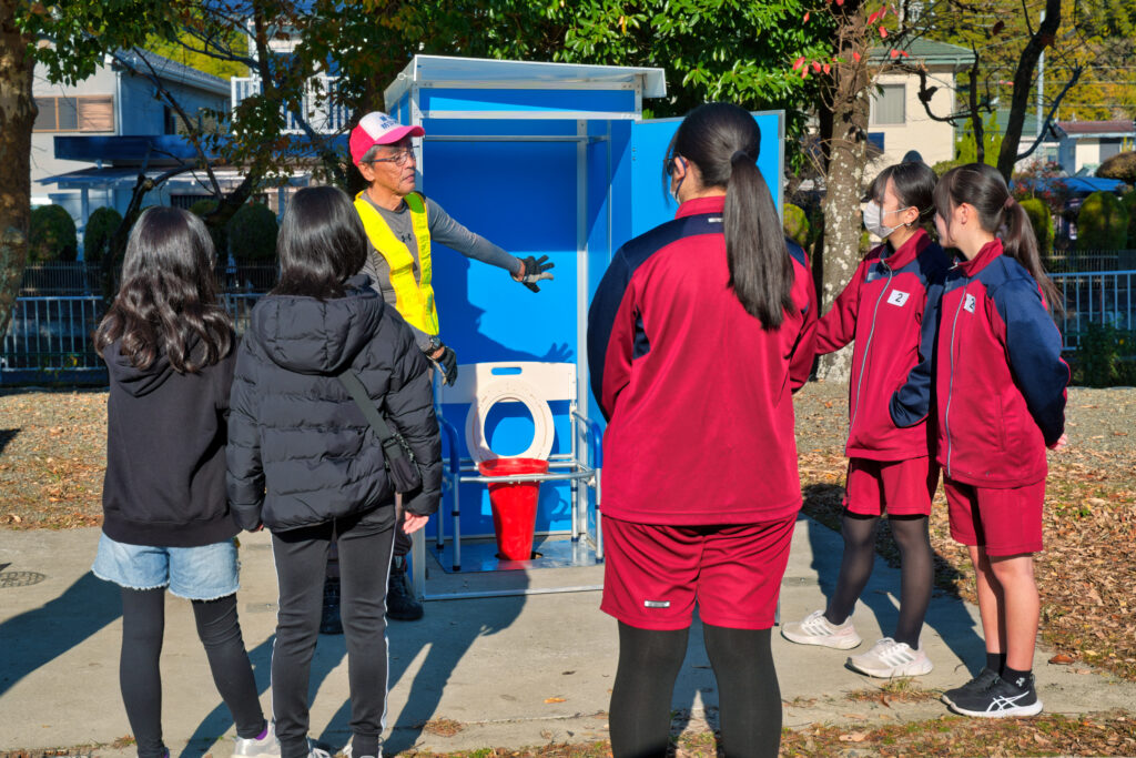 完成したマンホールトイレの前で役員から説明を受ける小中学生