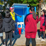 完成したマンホールトイレの前で役員から説明を受ける小中学生