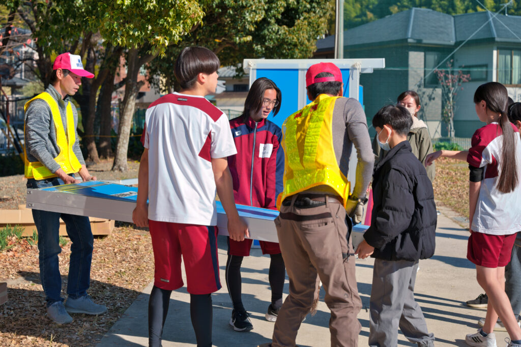 マンホールトイレの外装を運んでいる小中学生と役員たち