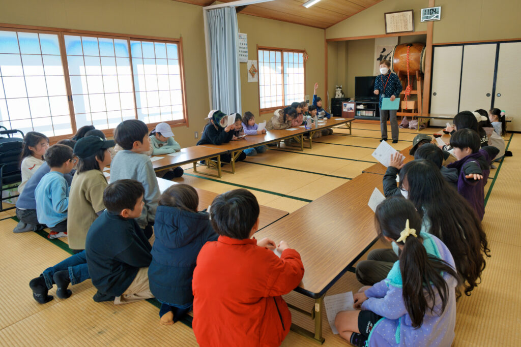 和室で七草粥の説明をする先生と、それを聞く子どもたち