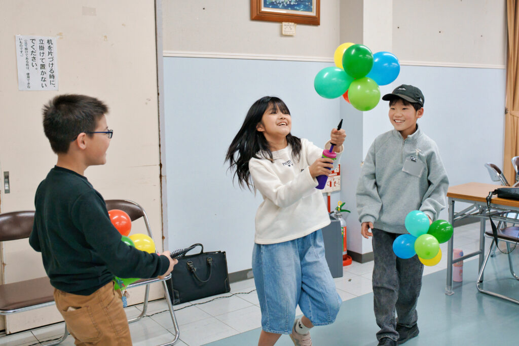 繋げた風船を空気入れで飛ばして遊ぶ子どもたち