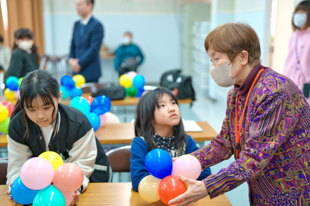繋げた風船を渡される子どもと、渡す代表の大畑さん