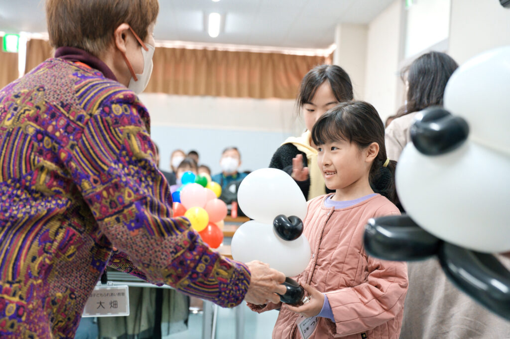 シマエナガのバルーンアートを手渡す代表の大畑さんと、嬉しそうに受け取る子どもたち