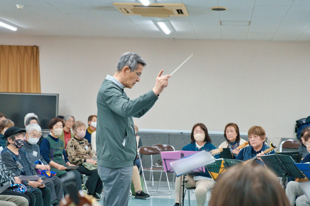 指揮に合わせ演奏するアンサンブルの方々と、聞く会員たち