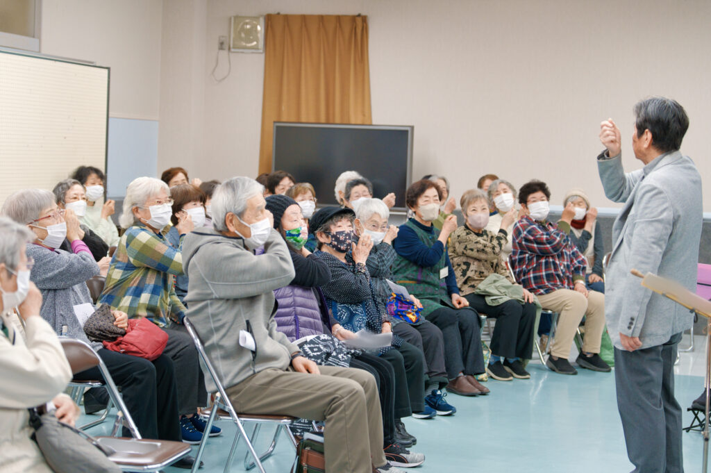 肩を叩くジェスチャーをする指揮者と会員たち