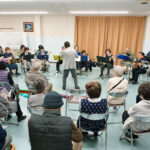 指揮に合わせ演奏するアンサンブルと、聞く会員たち