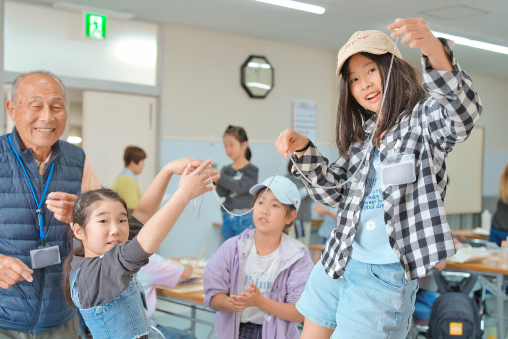 カメラ目線でスライムを細く長く伸ばしている子どもたち