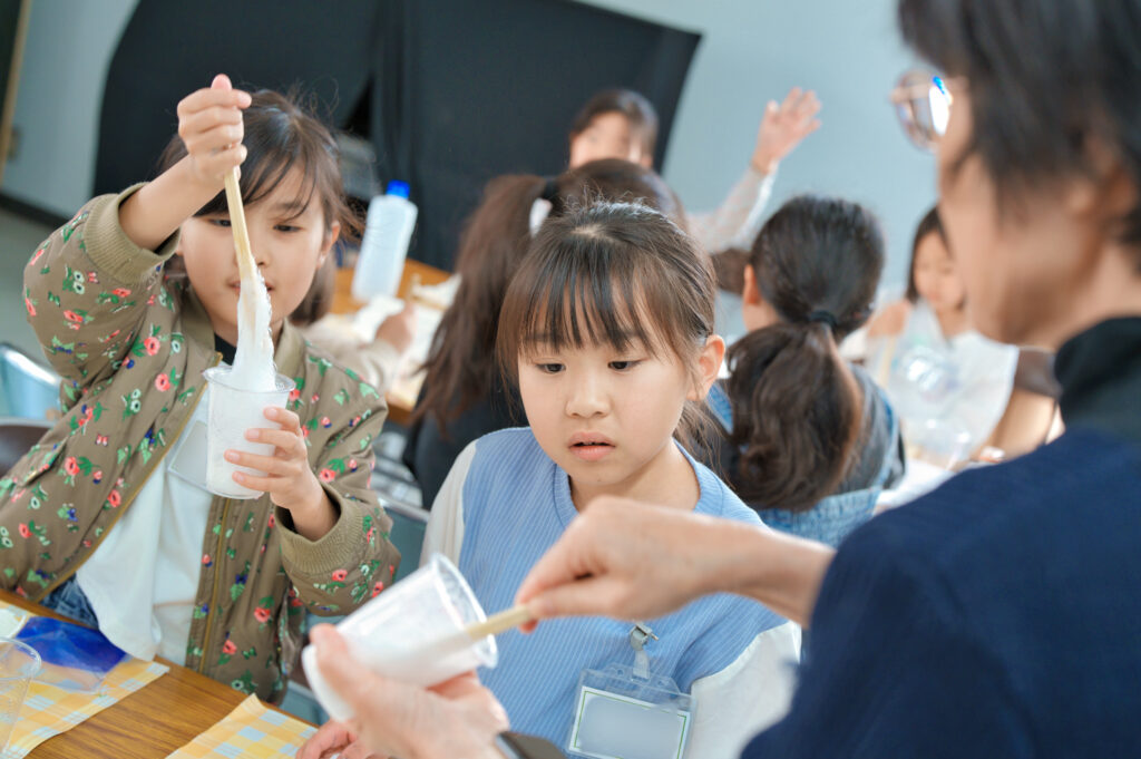 プラカップで割り箸を回し、ふわふわスライムを作ている子供たちと先生