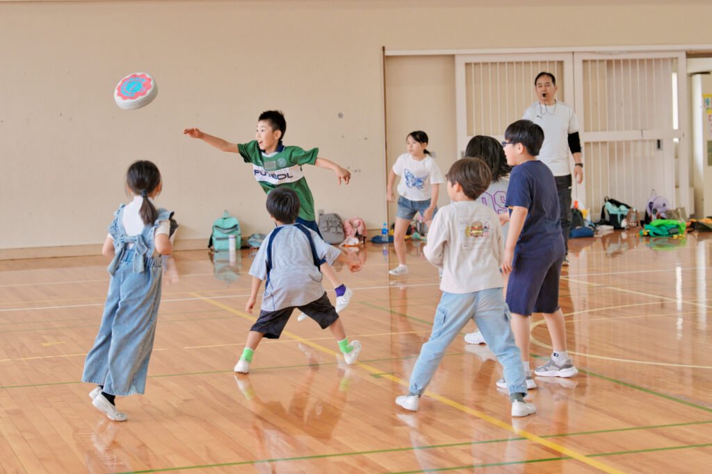 飛んで行くフリスビーを追う子どもと、それを注視する相手チームの子どもたち