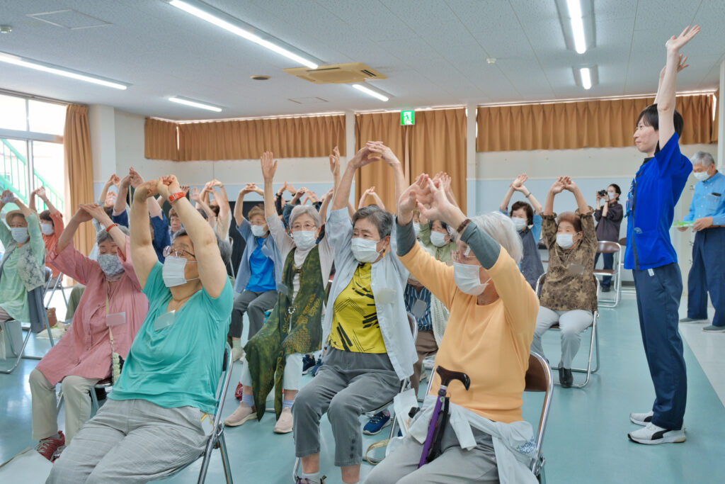 手を組み上に伸びる運動をする会員さんと、甲賀病院の方