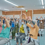 手を組み上に伸びる運動をする会員さんと、甲賀病院の方