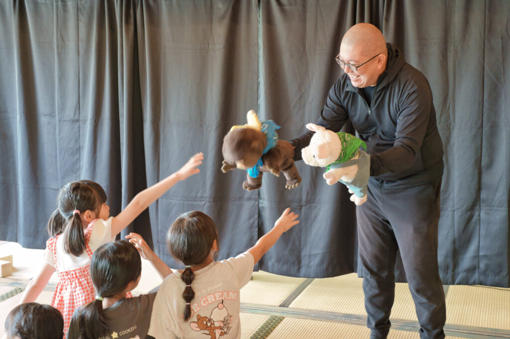 お坊さんが持つ人形を触ろうとする子どもたち