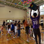 キリン先生が小さなボールをかごからばらまき、それを追う子どもたち