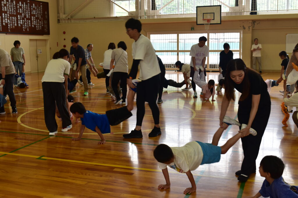 子どもたちがそれぞれの保護者に足を持たれ、手で移動している