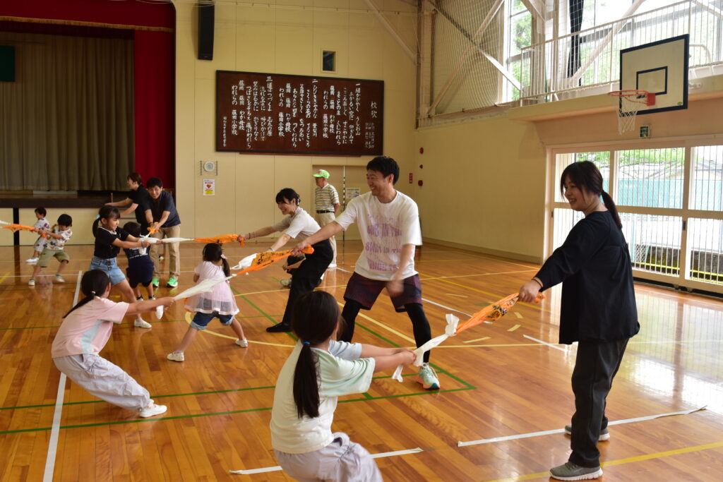 子どもたちがそれぞれの保護者と結んだタオルを引っ張り合っている