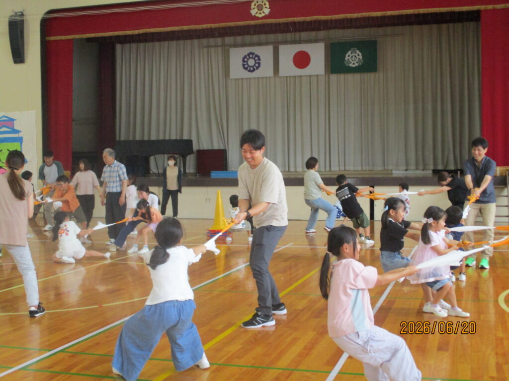 子どもたちがそれぞれの保護者と結んだタオルを引っ張り合っている