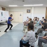 指を立てている塚本先生と会員たち
