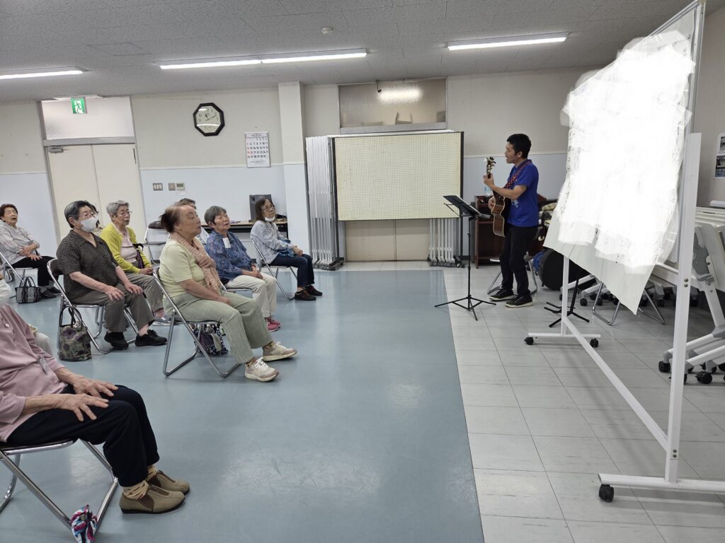 会員たちの前で弾き語りをする塚本先生
