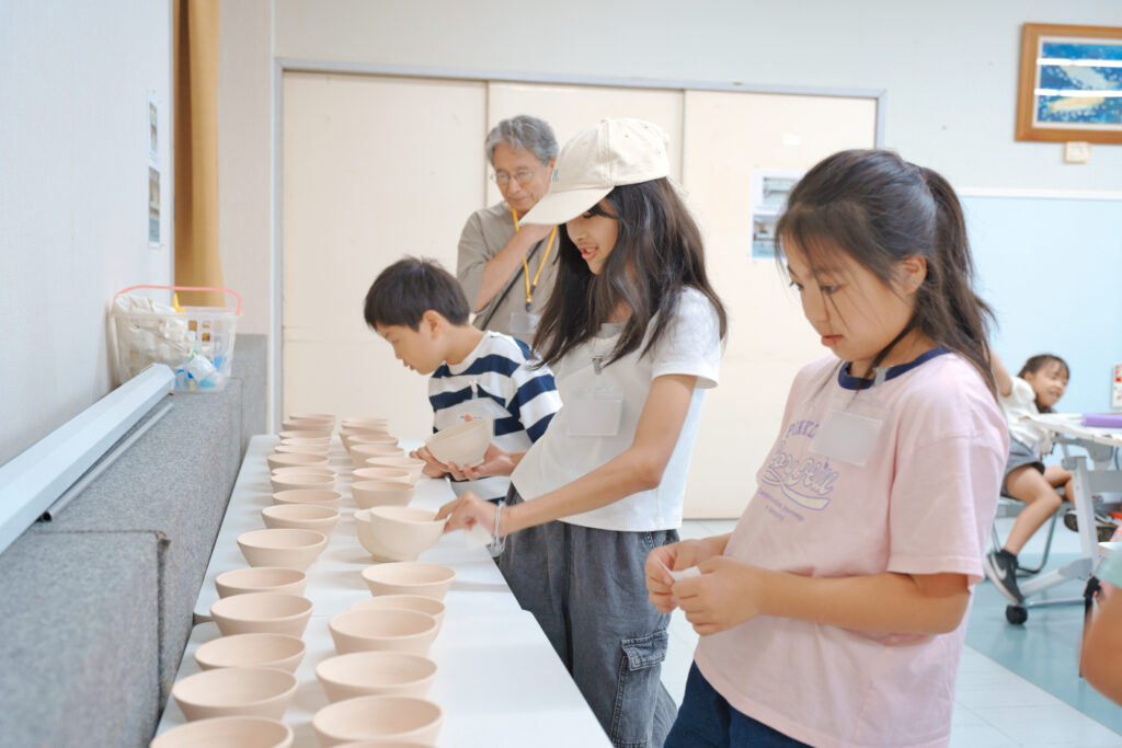 机に並んだ無地の器を選ぶ子どもたち