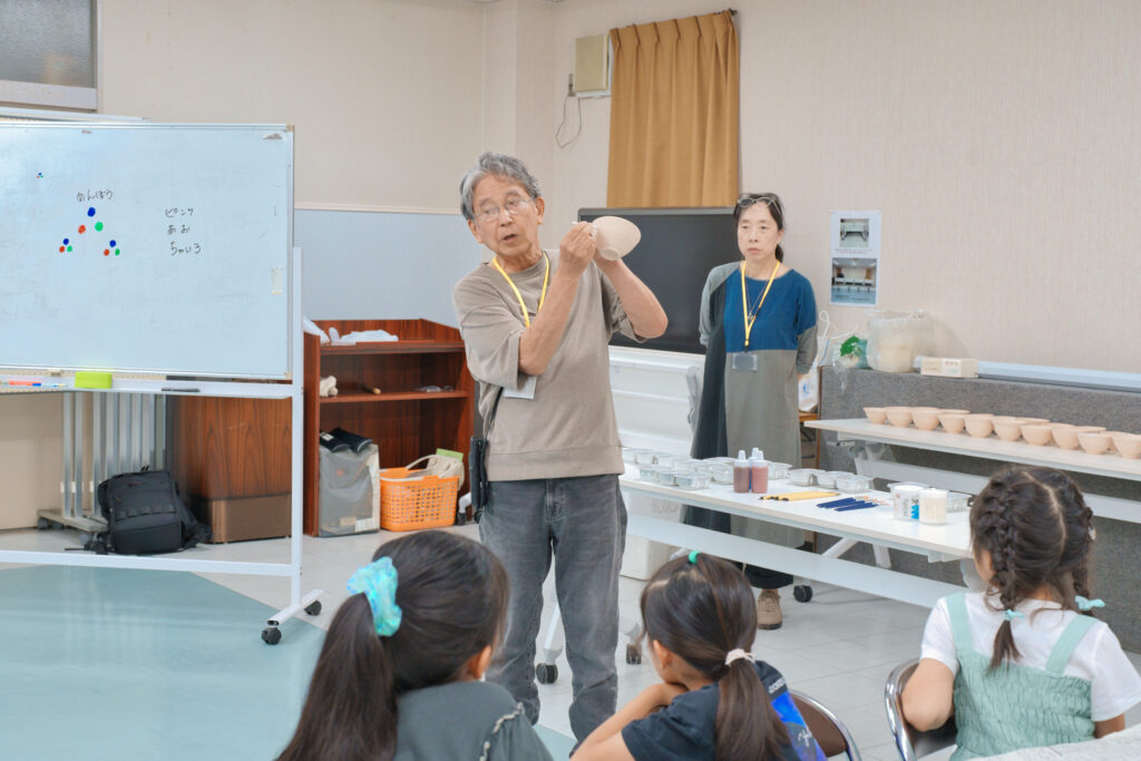 器を手に持ち解説する先生と、それを聞く子どもたち
